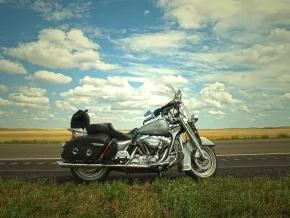 Egy ezüst színű motor a nyílt úton, háttérben felhős ég és aranysárga mezők.