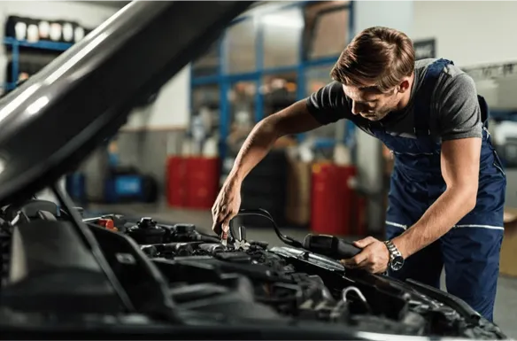 Mehaničar u radnji popravlja motor automobila koristeći alat.