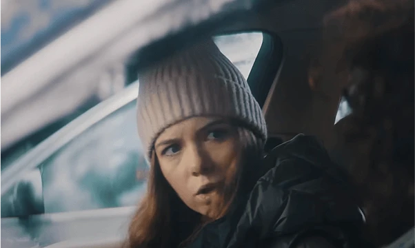 Osoba w białej czapce siedzi w aucie, twarz rozmyta, w tle wnętrze pojazdu i auto za oknem