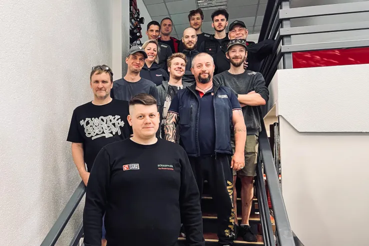 Vīriešu grupa pozē kāpņu telpā, tērpti sportiskos apģērbos.