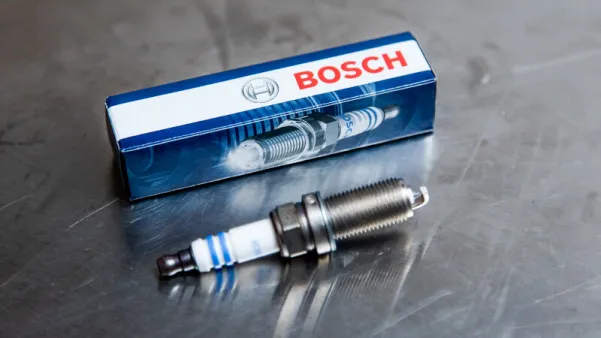 Bosch svjećica za automobil prikazana pored kutije na metalnoj površini.