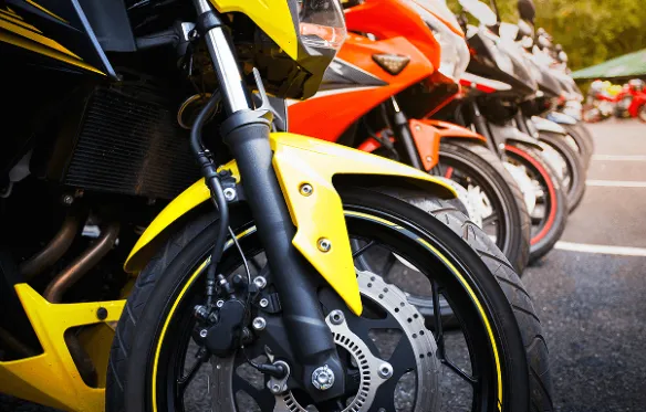 Prikaz prednjeg točka žutog motocikla u redu sa crvenim i crnim motociklima.