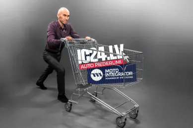 Vīrietis stumj iepirkumu ratus ar IC24.LV un Moto Integrator logotipiem.