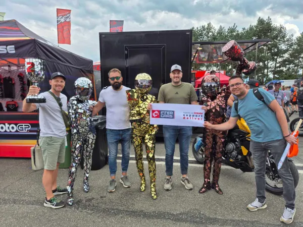 Grupa ljudi s Inter Cars banerom i trofejem pozira s figurama u sjajnim kostimima