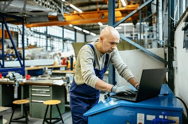 Un tehnician îmbrăcat în salopetă, lucrând la un laptop pe un birou de atelier.