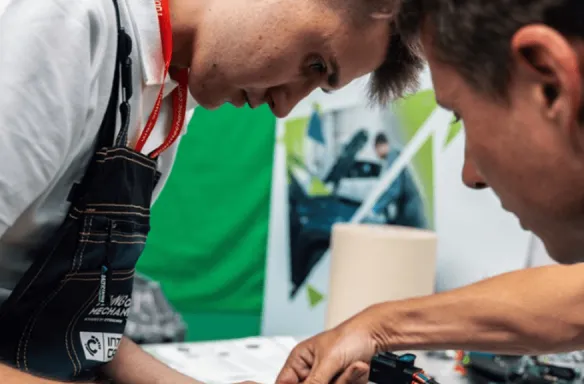Warsztaty mechaniki samochodowej Uczestnicy warsztatów mechaniki samochodowej pracują nad projektem, z narzędziami i materiałami na stole.