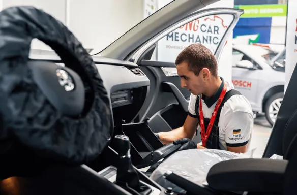 Mechanik samochodowy pracujący w samochodzie Mechanik w białej koszulce naprawia wnętrze samochodu, skupiony na pracy.