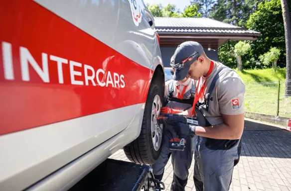 Pracownicy Intercars przy wymianie opony Pracownicy Intercars serwisują samochód, wymieniając oponę na zewnątrz w słoneczny dzień.