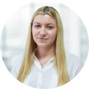 Kobieta w białej koszuli z długimi blond włosami, stojąca w jasnym otoczeniu biurowym.
