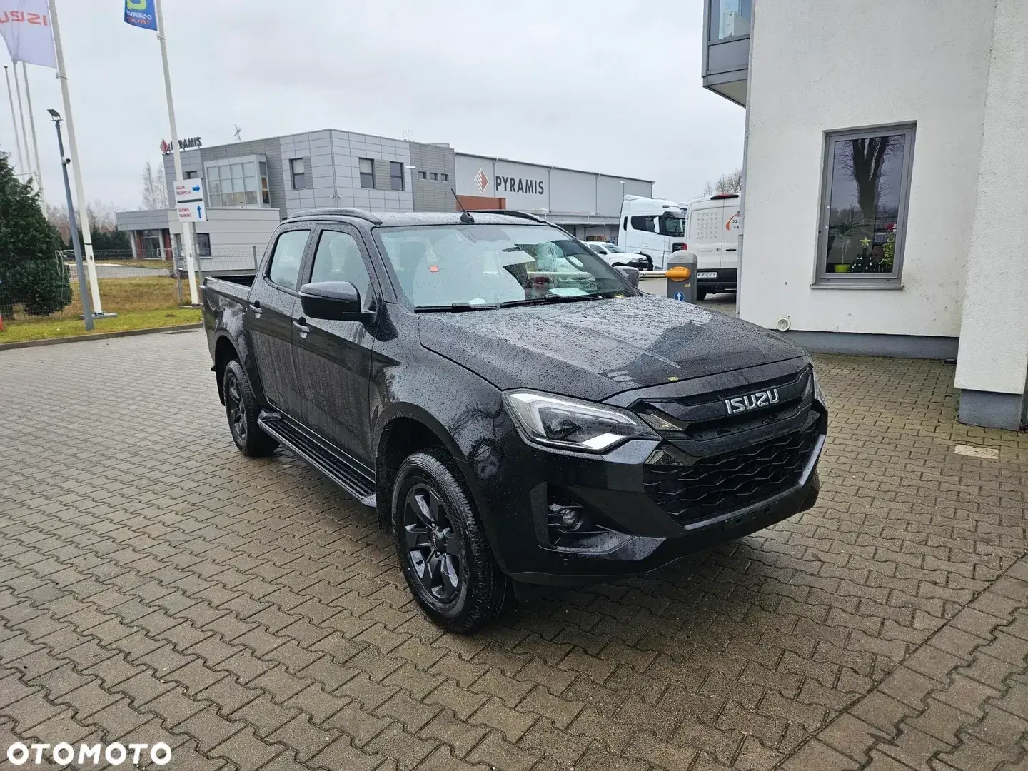 Czarny Isuzu D-Max zaparkowany przed salonem samochodowym.