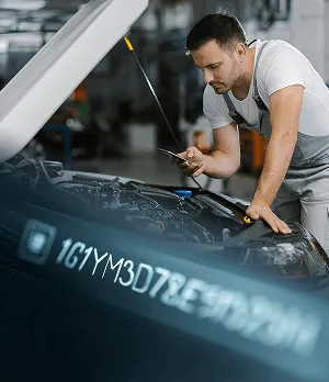 Механик работи по автомобил, проверявайки двигателя с телефон в ръка.
