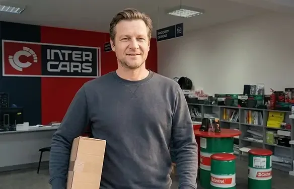 Mężczyzna w szarej bluzie trzyma paczkę w sklepie Inter Cars.
