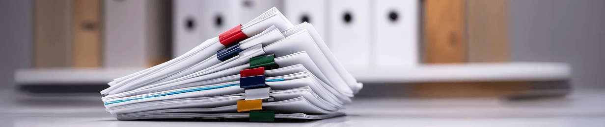 Un gruppo di documenti impilati con etichette colorate, sullo sfondo si vedono raccoglitori.