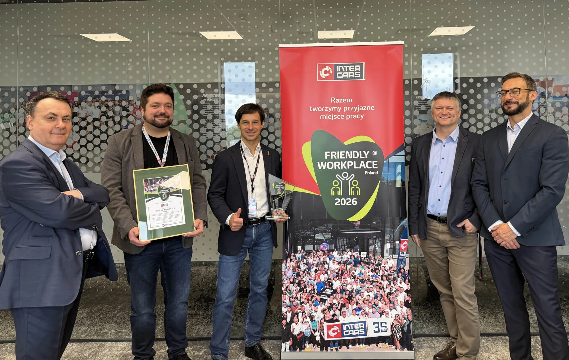 Pracownicy Inter Cars z nagrodą Friendly Workplace 2026 przy banerze firmy.
