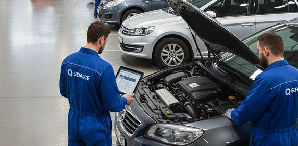 Du automobilių technikai apžiūri automobilio variklį su planšetiniu kompiuteriu servise.