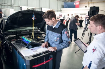 Mechanicy w warsztacie samochodowym używający specjalistycznego oprogramowania diagnostycznego na komputerze stacjonarnym do analizy danych z czarnego samochodu
