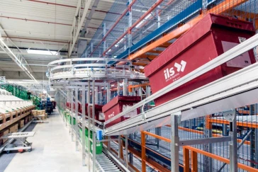 Wnętrze nowoczesnego magazynu z automatyzowanym systemem transportu towarów, z czerwonymi pojemnikami na regałach i metalowymi konstrukcjami