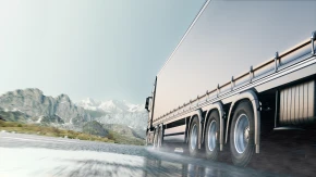 Truck Driving on Mountain Road A truck speeds along a wet mountain road with snow-capped peaks in the background.